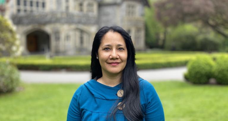 Assit. Prof. Athena Madan standing outside on the grass in front of Hatley Castle in a blue sweater.