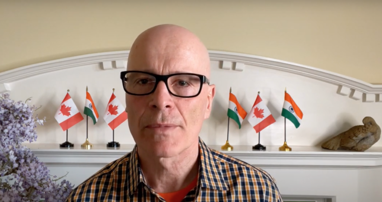 President Philip Steenkamp in front of mantle with Indian and Canadian flags.