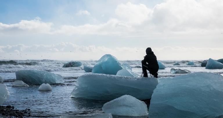 A person crouches down on an ice float. 