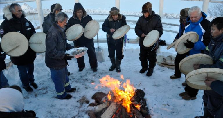 A group of people drumming around a fire on a snowy day