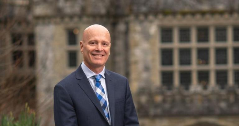 Smiling man in dark suit in front of grand old stone building