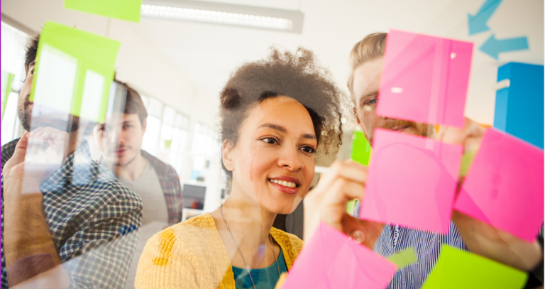 A group of people brainstorm on colourful post-it notes on a window.