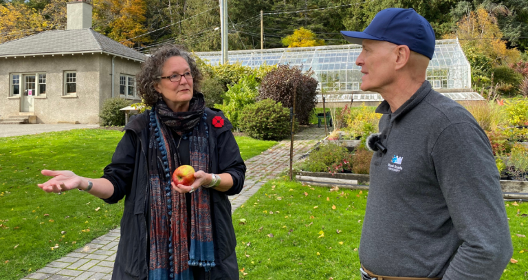 Two people, one holding an apple, in conversation in Royal Roads University's food garden.