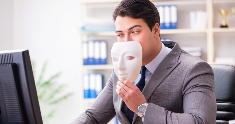 An investor looks at a computer screen with a mask that depicts a face lowered to partially reveal his face.