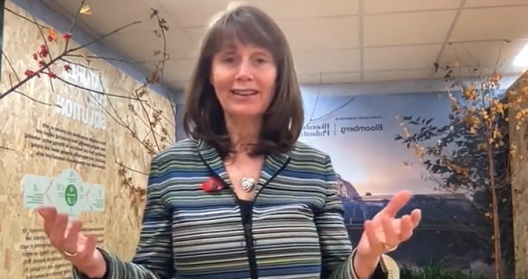 A woman speaks to the camera from the COP 26 conference in Glasgow with her hands raise, pals facing up.