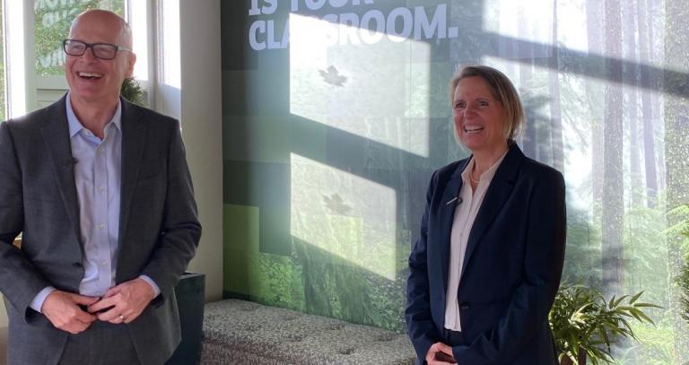 President Philip Steenkamp and Assoc. Prof. Kathy Bishop laugh together in a bright room with light pouring through the window.