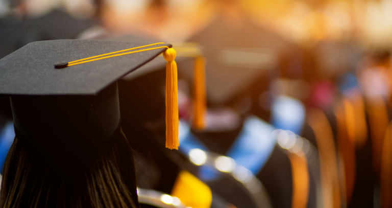 A line of graduates in cap and gown can be seen from behind.