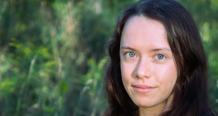 A head shot of a woman with greenery in the background.