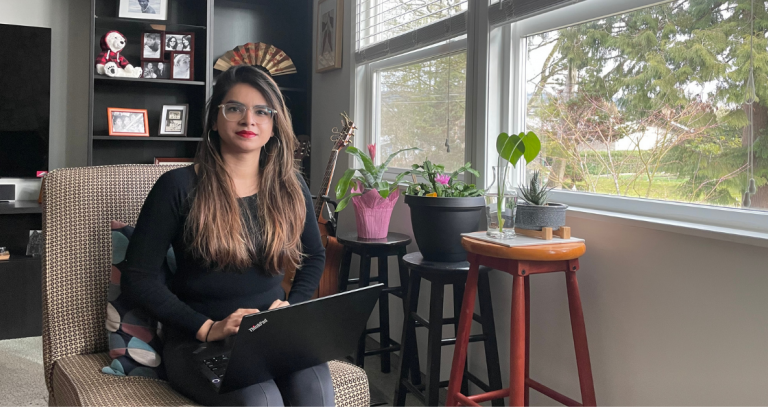 Eshwari Murumkar sitting on a chair with a computer on her lap, next to a large window to the right