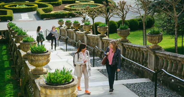 Two pairs of students walk up the flat, wide concrete steps of the Neptune Staircase on campus. Manicured hedges can be seen in the background.
