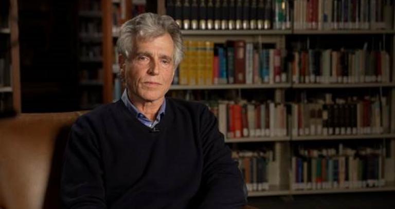 Dr. Thomas Homer-Doxon sits in a brown leather chair in the RRU Library.
