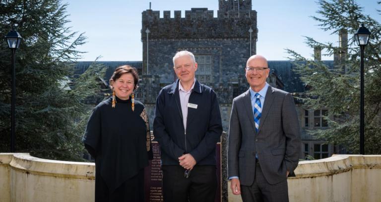 Deborah Saucier, President of Vancouver Island University, with Craig Davis, President and Head of College for Pearson and Philip Steenkamp, President and Vice-Chancellor of Royal Roads, stand together at the top of the Neptune Stairs. Hatley Castle is visible in the background. 