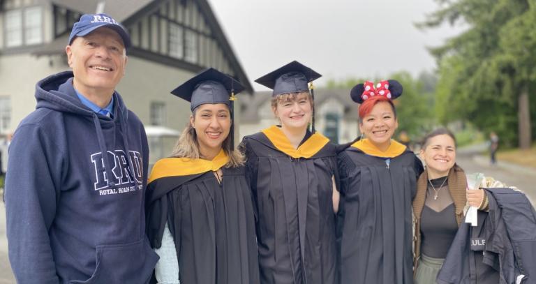 President Philip Steenkmap in an RRU hoody and hat, standing with three new graduates and a student.