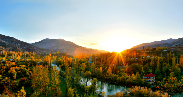 A setting sun peeks out from behind a forested mountain range.