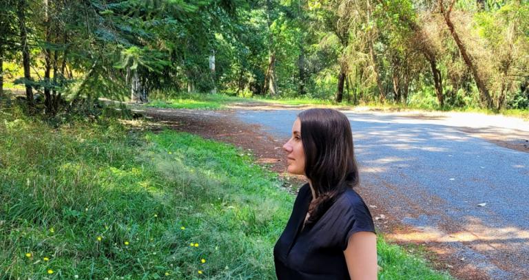 A woman stands near the forest looking into the distance
