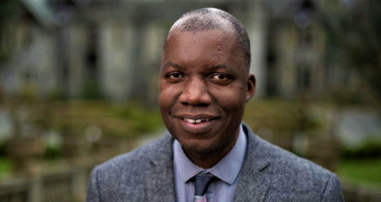 Nathan Banda stands in front of Hatley Castle, wearing a grey suit and tie