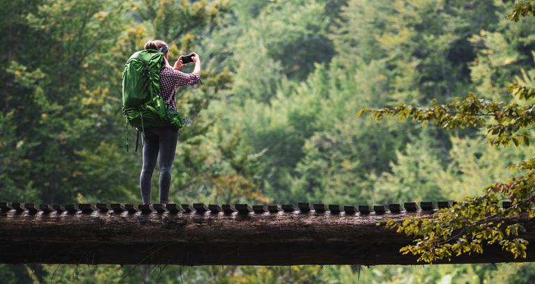 student taking a picture from a bridge, in nature