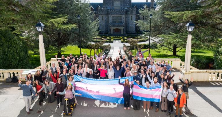 Dozens of people hold a giant trans flag outside of Hatley Castle in honour of Trans Day of Visibility.