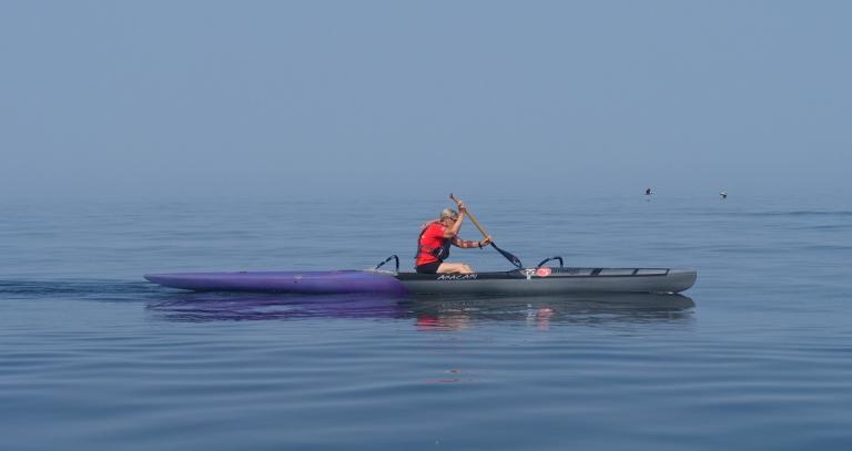 Woman in red shirt rowing in a boat with blue water below and blue sky above