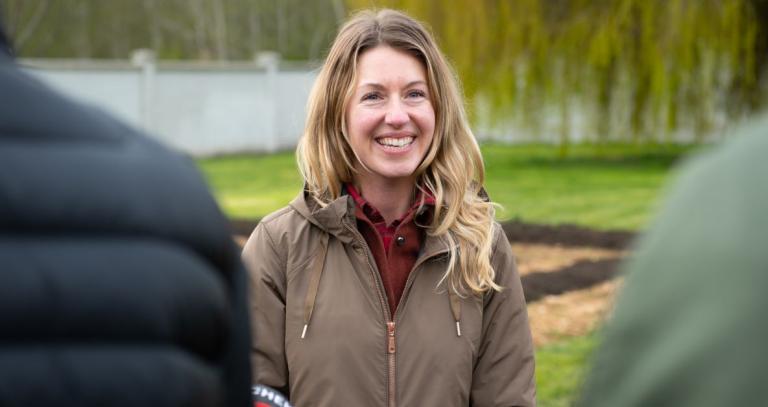 Solara Goldwynn smiling, as she is interviewed in front of the Royal Roads Giving Garden.