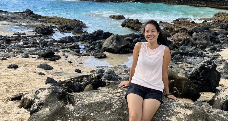 Vivan Giang sits on volcanic rock in front of the ocean.