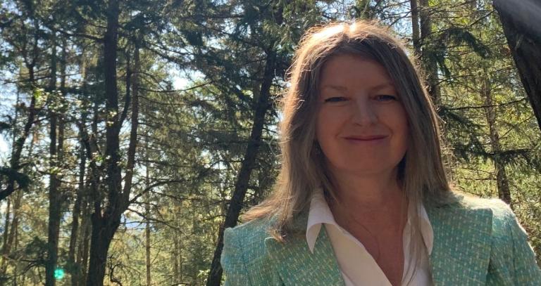 Woman in green suit jacket smiling with the sun shining behind her