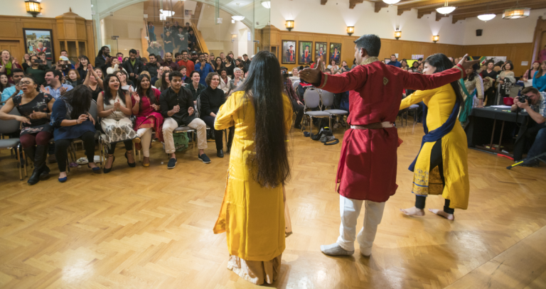 Three students in traditional cultural clothing dance in front of an audience of Royal Roads students and staff in the Grant Quarterdeck.