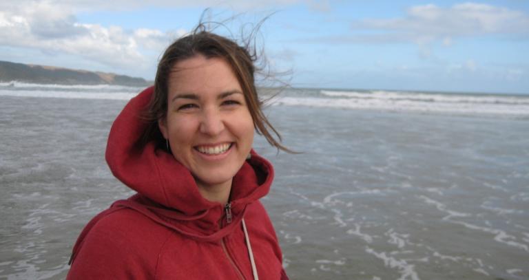 Julie MacArthur stands on an expansive beach, smiling. 