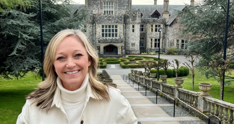 Sandra McDowell stands at the top of the Neptune Stairs, smiling with Hatley Castle in the background.