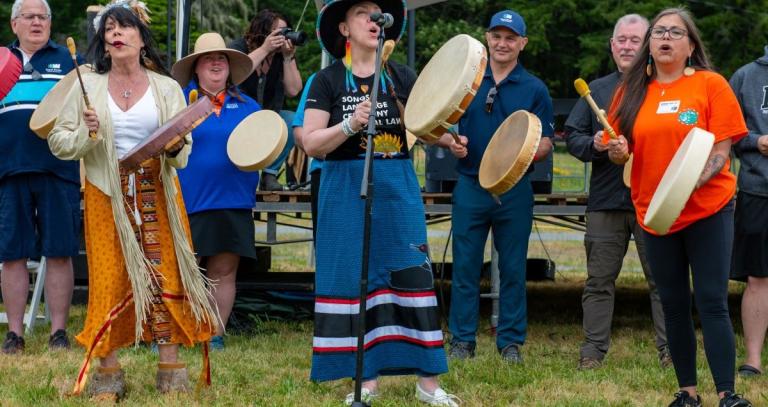 A group of people with drums sing near a microphone