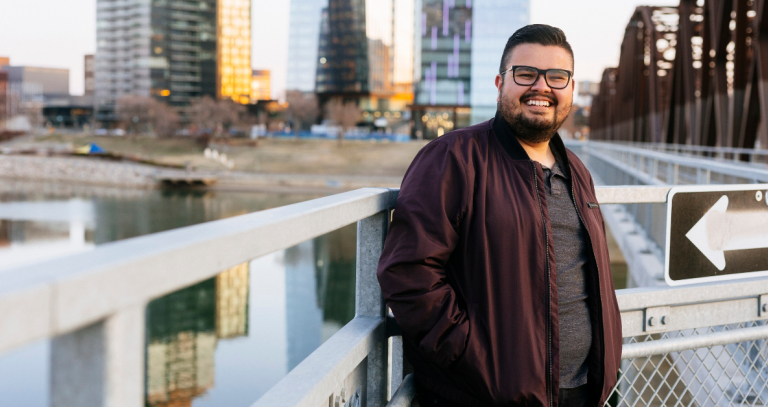 A man stands and poses for a picture against a cityscape.