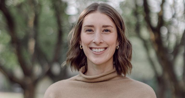 close up of woman smiling at the camera. She has short brown hair and is wearing a tan coloured shirt.