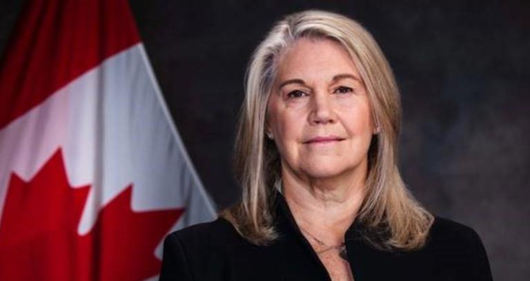 Jody Thomas stands in front of a Canadian flag. 