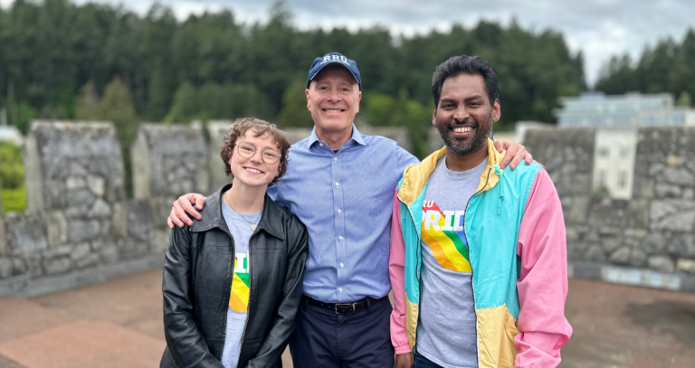 Students Kate and Richard with President Steenkamp on the top of Hatley Castle. The students are wearing pride shirts with cool jackets over them,