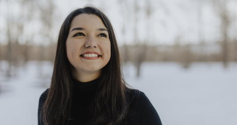 Andrea Juárez stands in front of a snowy background smiling. Photo credits to Aron Diaz. 