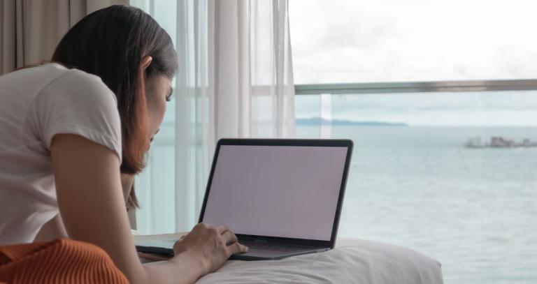 Women scrolls on laptop in front of ocean-view window