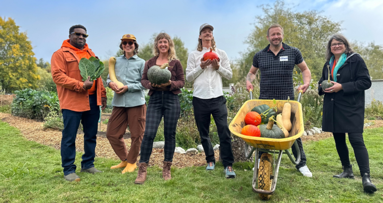People stand in front of a garden, squashes in hand
