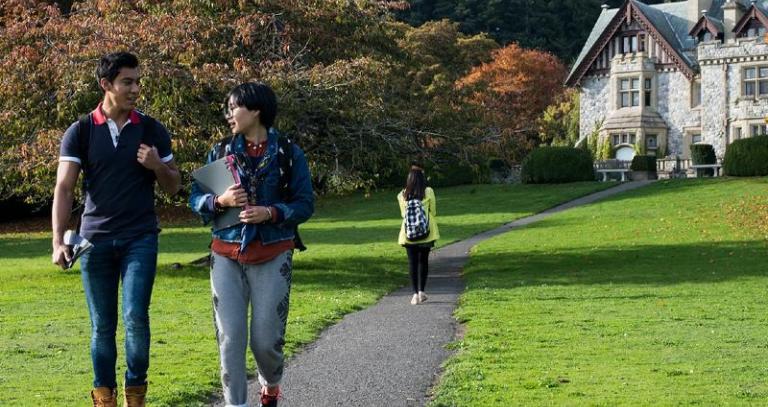 Two students walk side-by-side down a paved path at Royal Roads University.