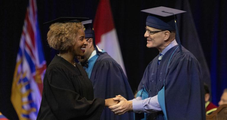 President Philip Steenkamp shakes the hand of a convocating student as they cross the stage.