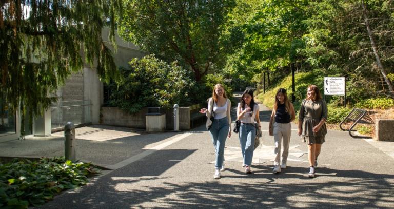 Four students walking and chatting in the tree lined boulevard outside the RRU Library.
