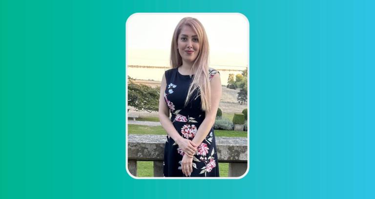 A woman stands on the terrace of Hatley Castle. In the background is a green lawn and the waters of the Esquimalt Lagoon.