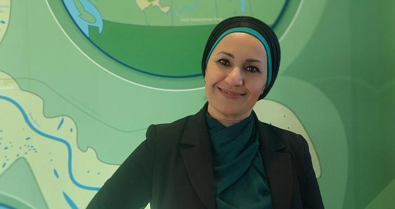 Wasan Jema, wearing a black head covering, stands in front a wavy green backdrop.