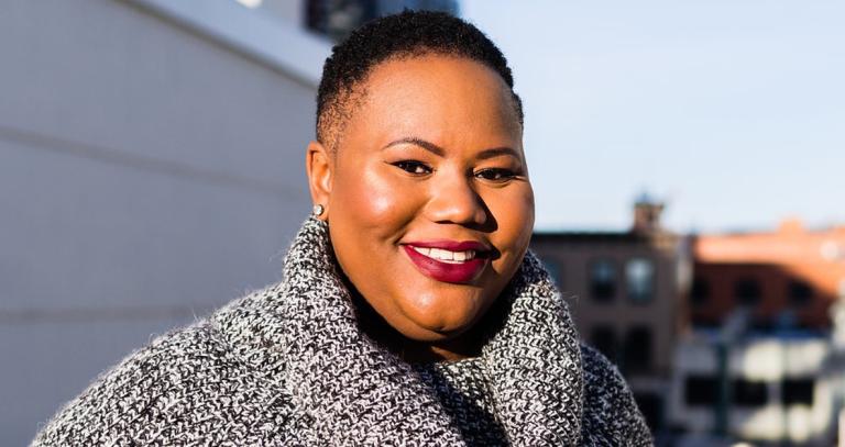 Isha Thompson smiling at the camera, wearing a black and white sweater.