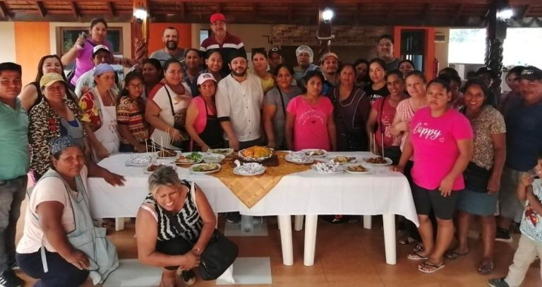 Large group of people standing around a table filled with various food dishes.