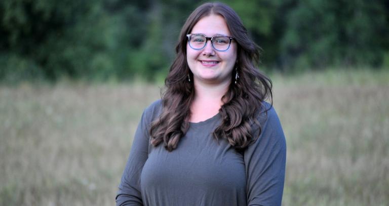 Leeza Perehudoff smiling at camera with a field of grass behind her. 