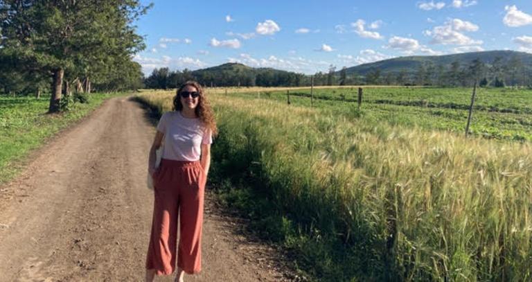 Emily Burkholder standing on a dirt road with a field of grass and rolling hills to her right.