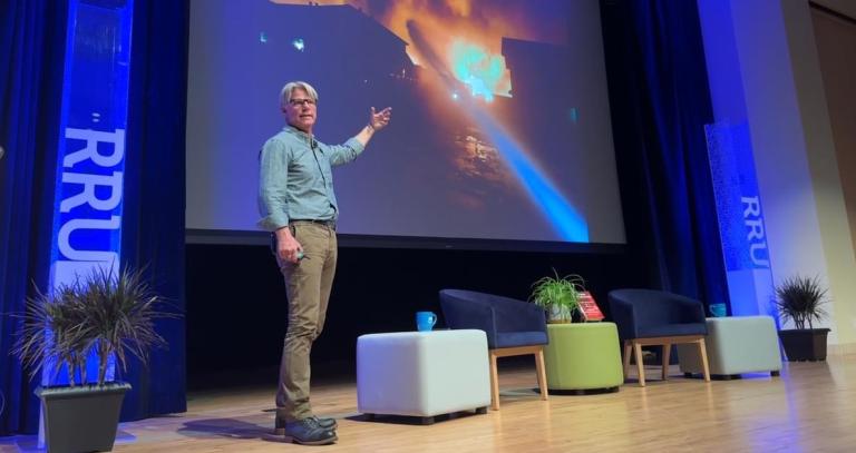 Author John Vaillant on stage pointing at an image of a blazing fire.