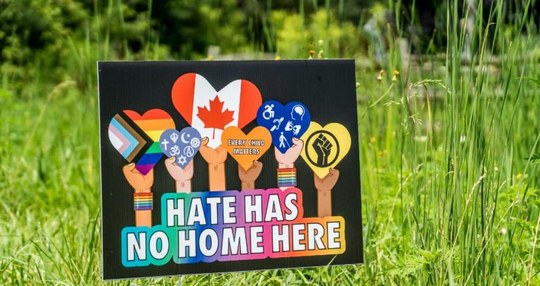 Hate has no home here lawn sign with images of hands holding up hearts.