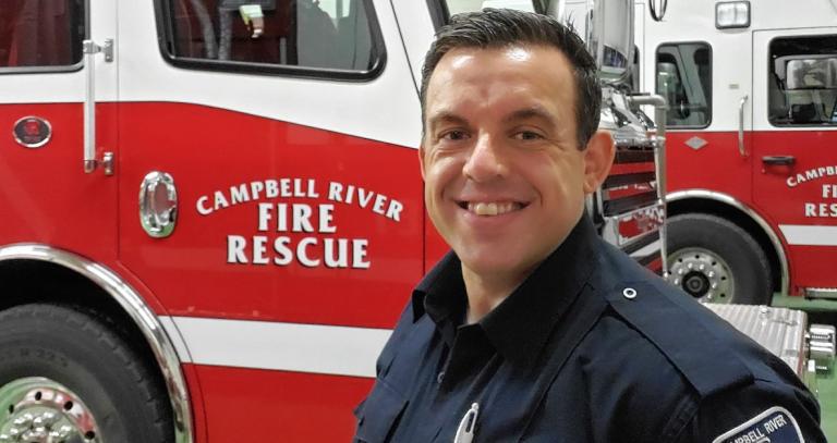Jesse Challoner smiling and standing in front of a Campbell River Fire Rescue truck.
