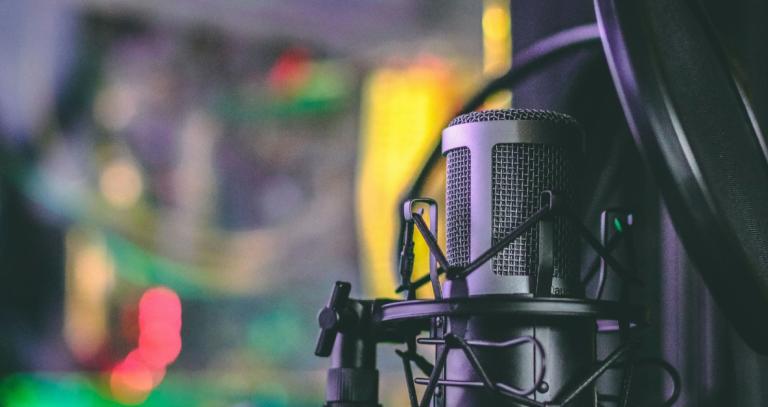 Close-up for microphone on a stand with blurred audio board in the background.